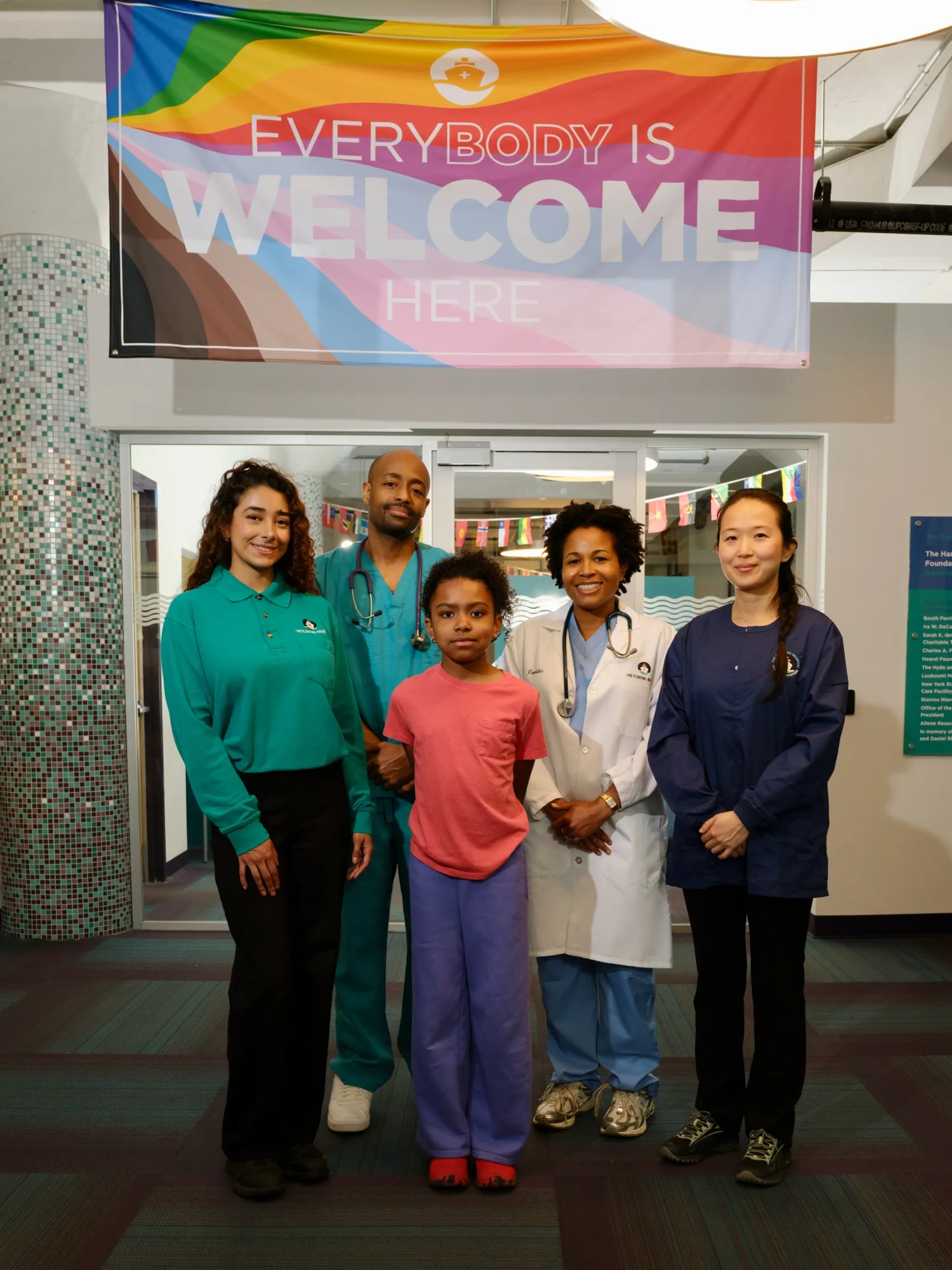 Four Floating Hospital staff members and a child beneath an Everybody Is Welcome banner