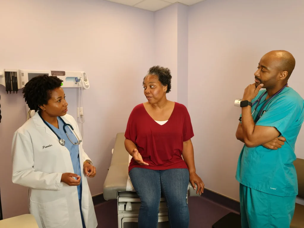 A doctor and nurse speak with a patient seated in an exam room
