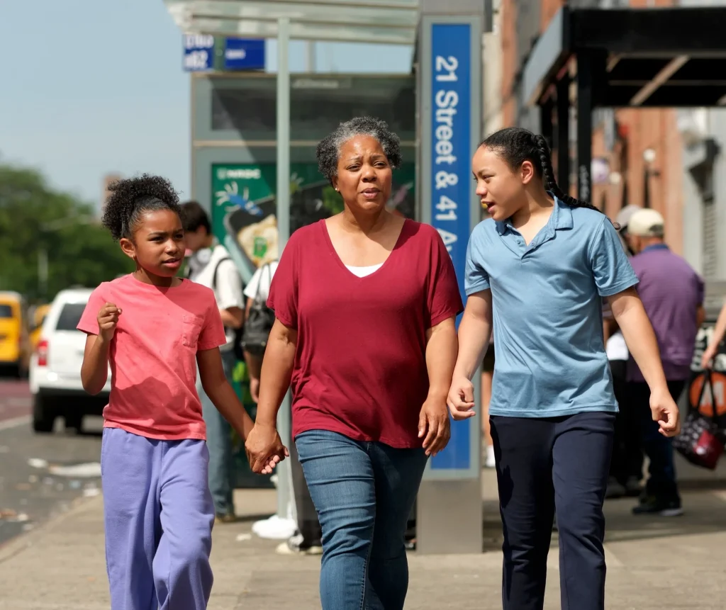 A woman walks with two children past a subway entrance in New York City