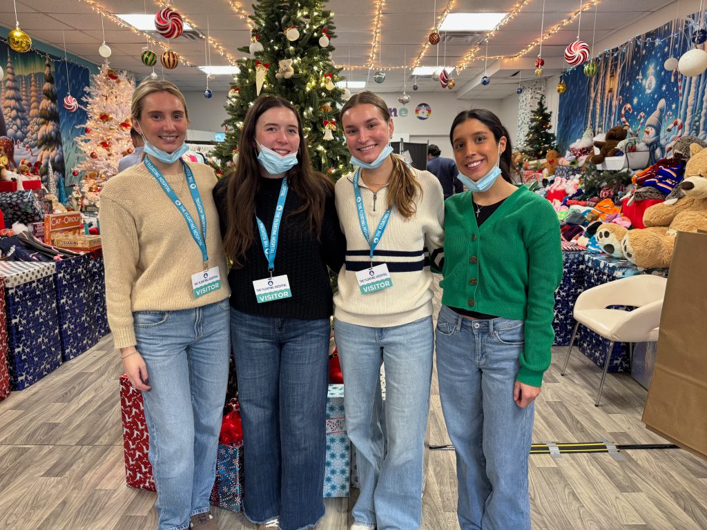 Four volunteers in visitor badges stand in front of a decorated holiday tree