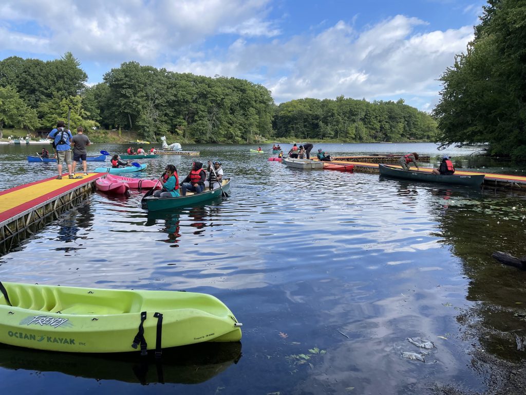 Campers paddle canoes and kayaks from a dock on a lake