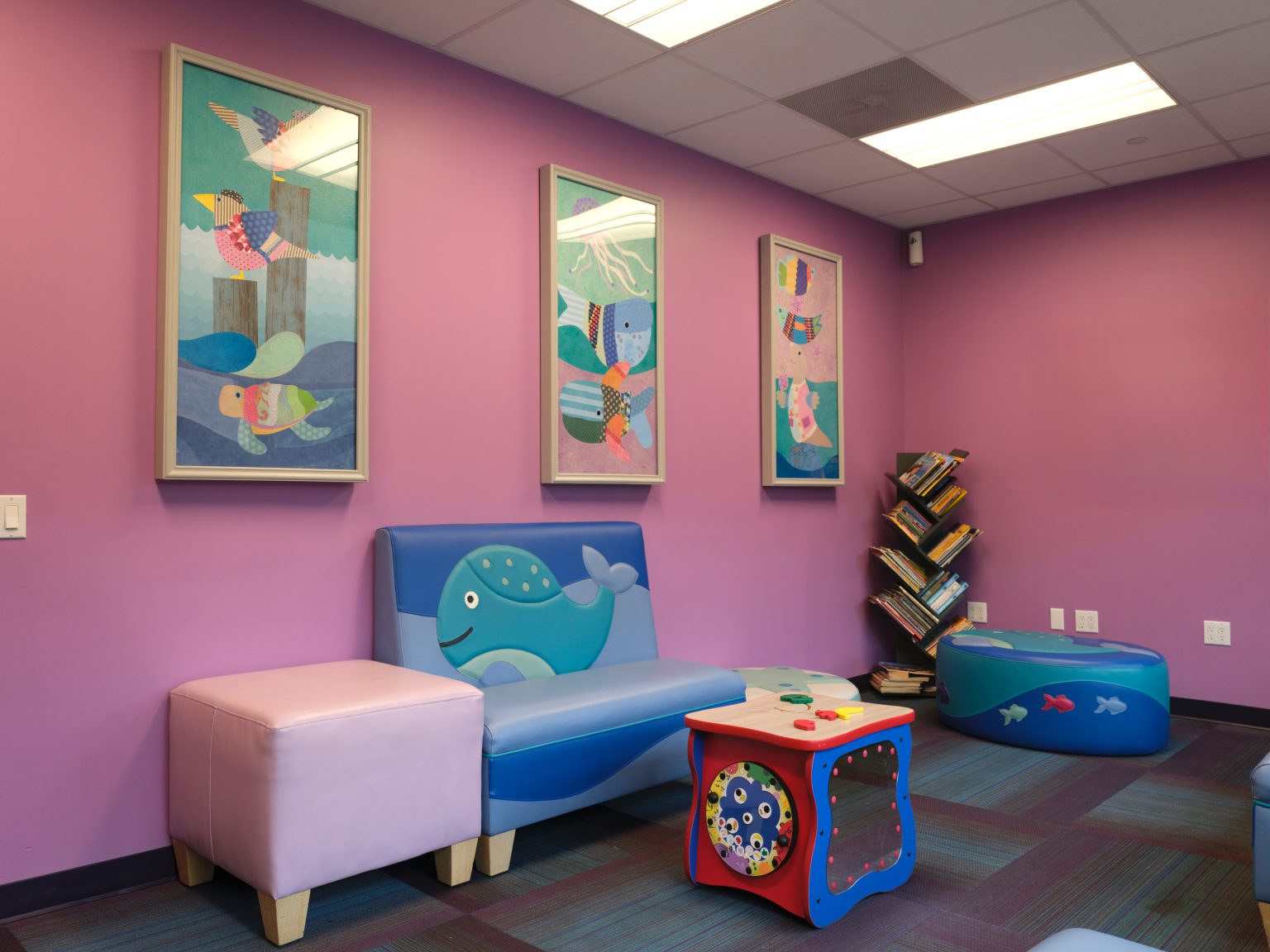 A brightly painted clinic play area with a whale bench and children’s books