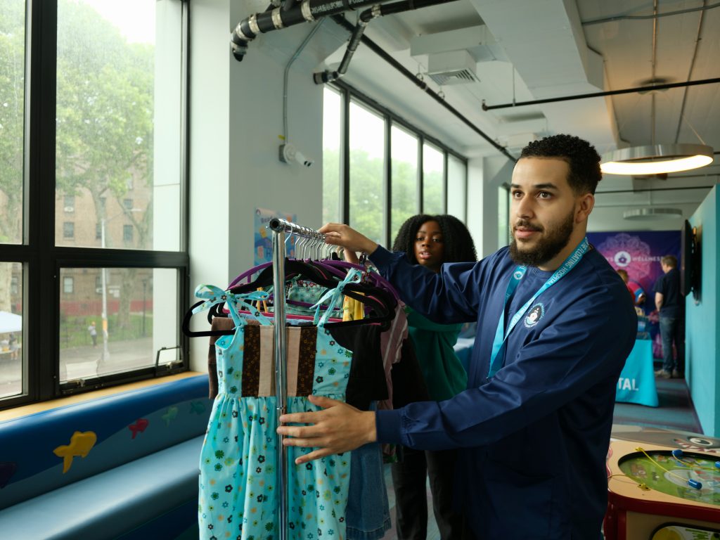 Two staff members hang donated children's clothing on a rack