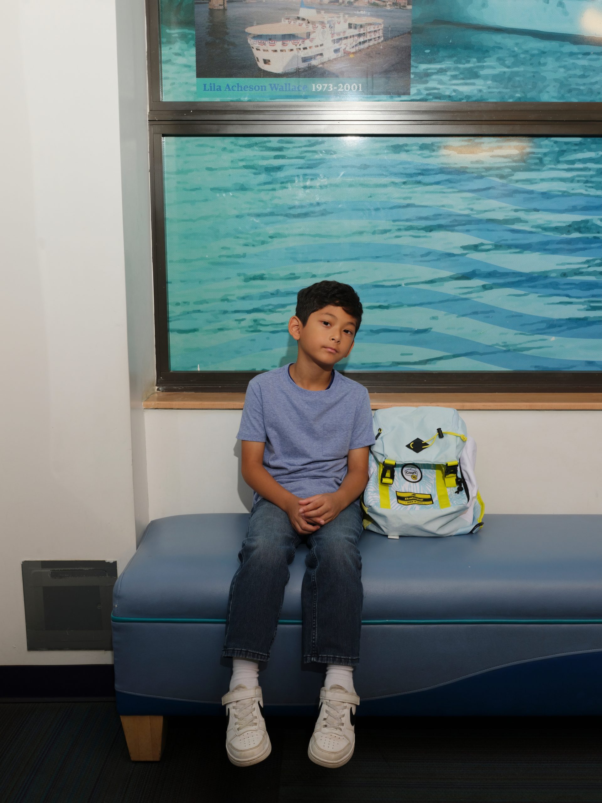 A boy sits on a bench with his backpack beside him